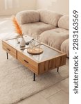 Small photo of Interior design of harmonized living room with design beige sofa carpet, coffee table, dried flowers in a vase and elegant personal accessories. Beige wall. Minimalist home decor. Modern concept