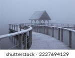 Scenic lake side view with wooden jetty in dense fog in winter.