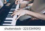 Small photo of Young bearded keyboardist is playing keyboard while his friends during rehearsal at home. Close shot of hands on key buttons.