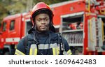 Small photo of Portrait of african american Firefighter in uniform and helmet near fire engine.