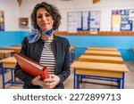 Caucasian female portrait of young teacher in class looking at camera, wearing a dark jacket and scarf. She has brown short curly hair. Educational background with copy space. Back to school concept.