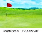 Small photo of Golf field. Green grass against the background of the sea shore and the blue sky. Signal flag for the hole on the golf course