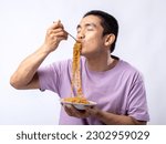 A portrait of a happy Asian man wearing a purple shirt while eating noodles. Isolated with a white background.