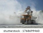 Excavator and mining truck in a cloud of stone dust, loading of a small fraction of stones in slate quarry, close-up.