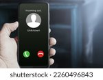 Small photo of Male hand holding mobile phone showing incoming call from an unknown caller on the screen, with buttons to answer or reject. Possible scammer or spam call. Mobile security and privacy concept.