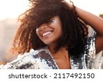 Portrait of overjoyed glamour african american woman with glitter on face in silver sequin dress enjoying outdoor party or event, mixed race female in festive wear with eyes closed feeling happy