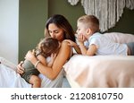 Young family beautiful mother with two son of different ages spending time at home, loving mom holding baby in hands and putting him to sleep with help and support of older child