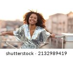 Outdoor portrait of happy glamour african american woman with glitter on face wearing festive wear sequin dress standing on roof terrace during party or celebration and smiling happily at camera