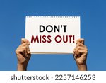 Small photo of Don't miss out message on a notebook paper held by 2 hands with blue sky background. This text can be used for business concept to inform customer.