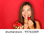 Girl eating strawberries smiling happy looking to the side on red background with copy space. Beautiful young mixed race Asian and Caucasian woman eating healthy.