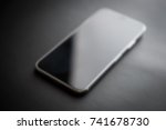 Modern mobile device like iPhone XS model.New smartphone blur background.Out of focus cellphone with big infinity edge display.Touchscreen panel on black background