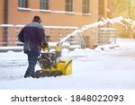 Worker with track drive snow thrower removing deep snow, heavy duty assistant for snow and ice removal in winter season. Motor machine for removing deep, wet, heavy snow. Snowblower equipment