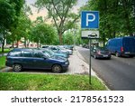 Parking lot sign, cars parked under green trees in residential area, Parking zone. Parking problems not enough free space. Crowded public parking lot on narrow street. Rows of cars parked on roadside