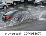Small photo of Car splashing water, driving through puddle at heavy rain. Car driving on flooded asphalt road at heavy rain, wet road. Dangerous driving conditions, risk of aquaplaning. MOTION BLUR.
