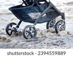 Small photo of Baby stroller on wet snow in winter season. Baby carriage stand on slushy snowy road during heavy snowfall in the city, walking problem in winter. Wheels of the baby stroller stuck on sleet