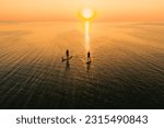 Aerial view of two people on stand up paddle boards on quiet sea at sunset. Warm summer beach vacation holiday. Active leisure on a seaside.