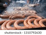 Street Food Market Vendor Cooking and Selling Sausages. Tasty Sausages on Large Commercial Griddle Hotplate. Street Food Cooking on Big Frying Pan Outdoor. Tongs In Hand Holding Sausages.