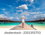 Beautiful young woman in front of water luxury villas standing on the tropical beach jetty (wooden pier) in Maldives island
