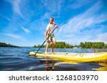 Happy man is paddling on a SUP board on a large river at sunny day. Stand up paddle boarding - awesome active recreation in nature.  Wide angle.