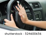 Closeup inside vehicle of hand pushing on steering wheel honking horn, black interior background, female driver concept