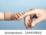 Closeup of a baby holding man's finger against blue background