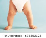 Low section of baby boy in diaper standing isolated on blue background