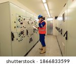 Small photo of Worker stay in large control room. Power Plant Control Panels with schema. Engineer standing in front of the control panel, check the values and phoning with the supervisor room.