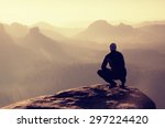 Young man in black sportswear is sitting on cliff's edge and looking to misty valley bellow. Autumn landscape. Foggy mountain.Person look. Man hike.Cliff edge. Climbing adventure.Guy look.Foggy valley