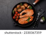 Grilled salmon steaks and potatoes sizzling in a frying pan, a mouthwatering delight. Flat lay with copy space