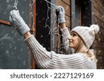 holiday decorations. woman install electric christmas string lights on house exterior facade