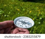 Small photo of A compass in person's hand in park with flowers. Orient yourself in current situation (urban conditions). Follow innner compass, intuition concept, public sentiments