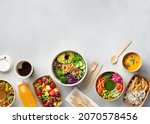 Healthy take away food and drinks in disposable eco friendly paper containers on gray background, top view. Fresh salad, soup, poke bowl, buddha bowl, fruits, coffee and juice.