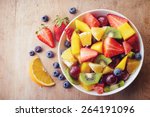 Bowl of healthy fresh fruit salad on wooden background. Top view.