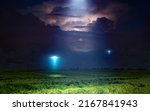 Small photo of Fantastic dramatic image: UFO or alien spacecraft inspect green grass field with bright spotlight in dark stormy night sky.