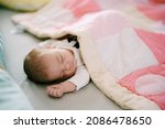 Small photo of Baby sleeps on bed covered with pink patchwork quilt