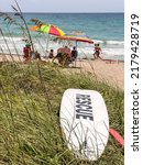 Small photo of HUTCHINSON ISLAND, FLORIDA, USA - JULY 1, 2022: Lifeguards (off camera) keep a rescue board at the ready on dune grass near beachgoers on an uneventful afternoon at Sea Turtle Beach. Foreground focus.
