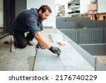 Small photo of industrial worker, handyman installing big ceramic tiles on bathroom walls. Balcony area covered in ceramic tiles with strong adhesive