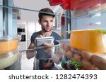 Close-up Of Man Writing On Spiral Book Near Open Refrigerator In Kitchen