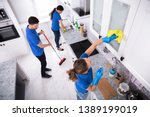 Group Of Young Janitors In Uniform Cleaning Kitchen At Home