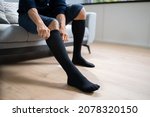 Man Putting On Medical Compression Stockings On Legs