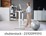 Woman Using Adjustable Height Standing Desk In Office For Good Posture