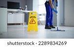 Small photo of Low Section Of Male Janitor Cleaning Floor With Caution Wet Floor Sign In Office