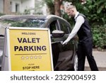 Small photo of Man Giving Car Key To Male Valet Near Valet Parking Sign
