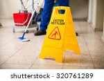 Low Section Of Worker Mopping Floor With Wet Floor Caution Sign On Floor