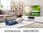 Young Woman Lying On White Carpet Holding Remote Control Enjoying Watching Television At Home