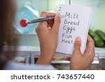 Close-up Of Woman Holding Spiral Book With Check List Against Open Refrigerator At Home