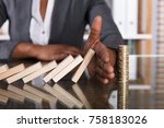 Close-up Of A Human Hand Stopping Wooden Blocks From Falling On Stacked Coins Over Desk