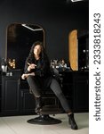 Small photo of Beautiful young brutal woman male master hairdresser, barber holding razor sitting on a chair in a hair salon