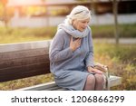 Senior Woman Suffering From Chest Pain While Sitting On Bench