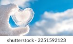 Small photo of frozen icy heart hand, winter background against clear blue sky and clouds, concept love, romantic, February 14, Valentine's day. festive winter season. Christmas New Year holiday. approach of spring